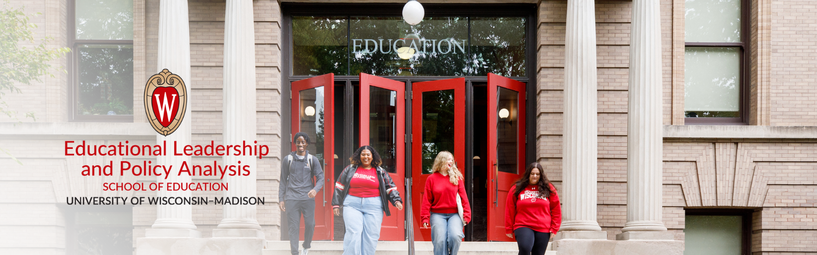 Four students, wearing red school apparel walk in front of open red doors.
