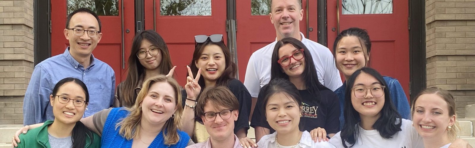 A group of 12 individuals pose in front of red doors.
